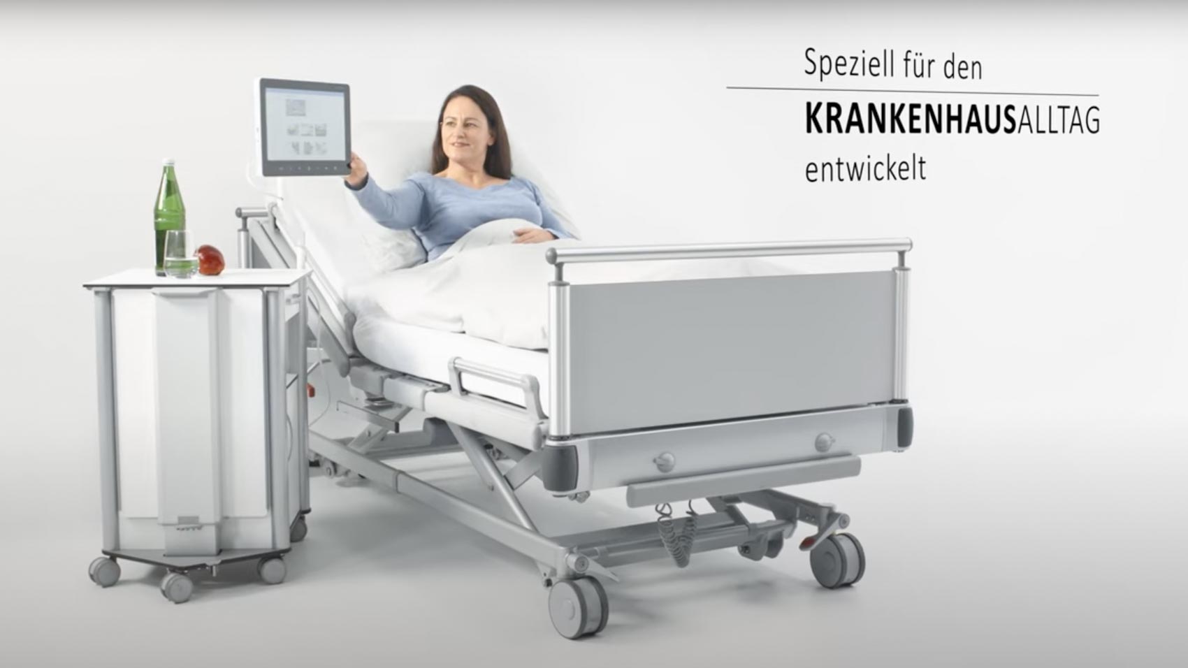 ConnectedCare.Nachttischschwenkarm GFK – Patientin im Krankenhausbett dreht Bedside Terminal an Nachttischhalterung