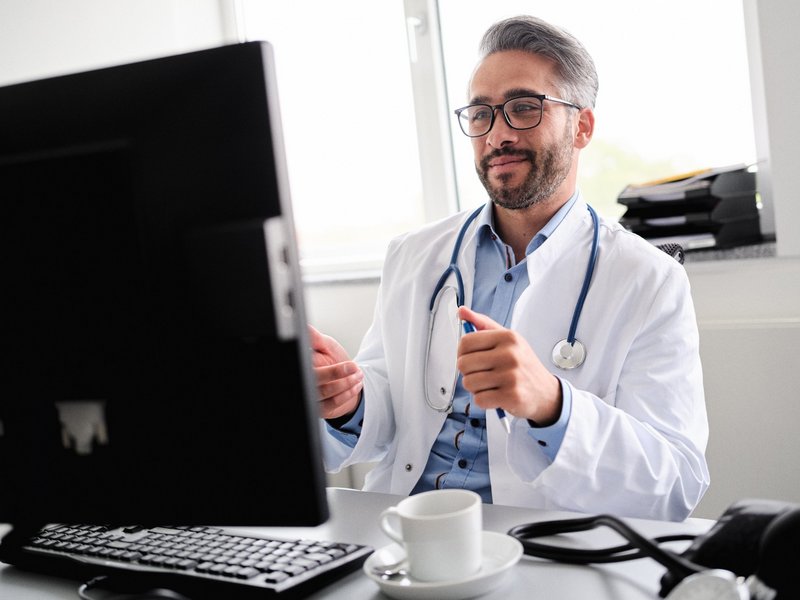Arzt sitzt am Rechner und hält Video-Visite mit Patienten