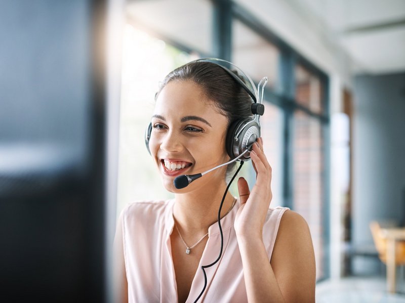 ConnectedCare Kontakt, junge Frau sitzt lächelnd am Computer und telefoniert über ein Headset