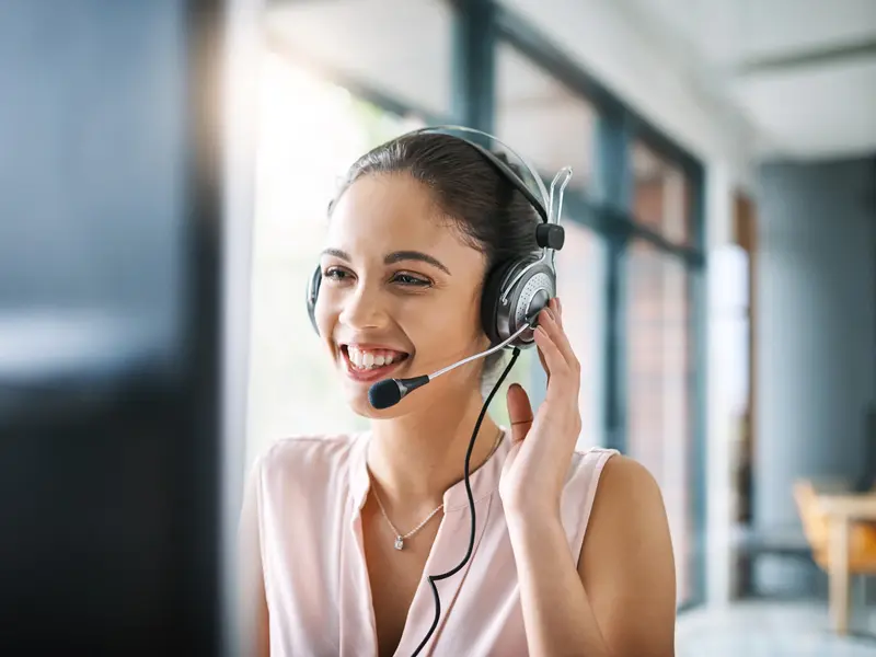 ConnectedCare Kontakt, junge Frau sitzt lächelnd am Computer und telefoniert über ein Headset