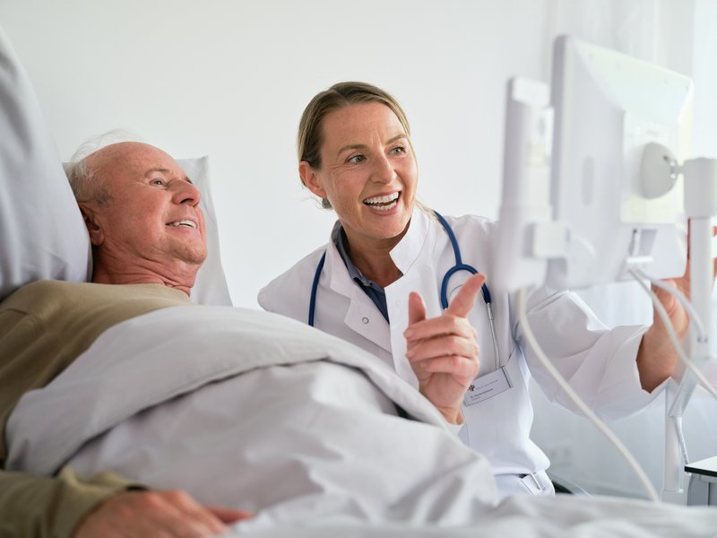 Digitale Kommunikation: Ärztin und Patient schauen fröhlich auf Bedside Terminal