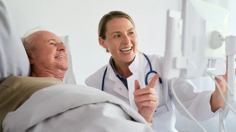 Digitale Kommunikation: Ärztin und Patient schauen fröhlich auf Bedside Terminal