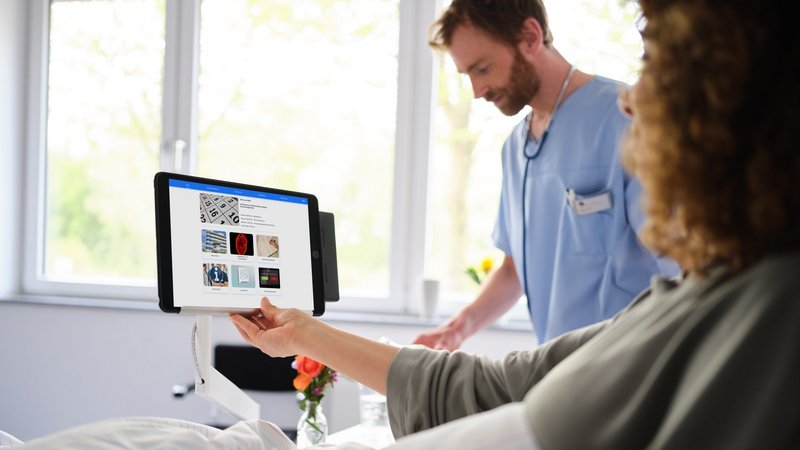 Krankenhaus digitalisieren: Patientin im Krankenhausbett bedient iPad mit eHealth Plattform ConnectedCare, ConnectedCare iPad-Halterung am Nachttisch